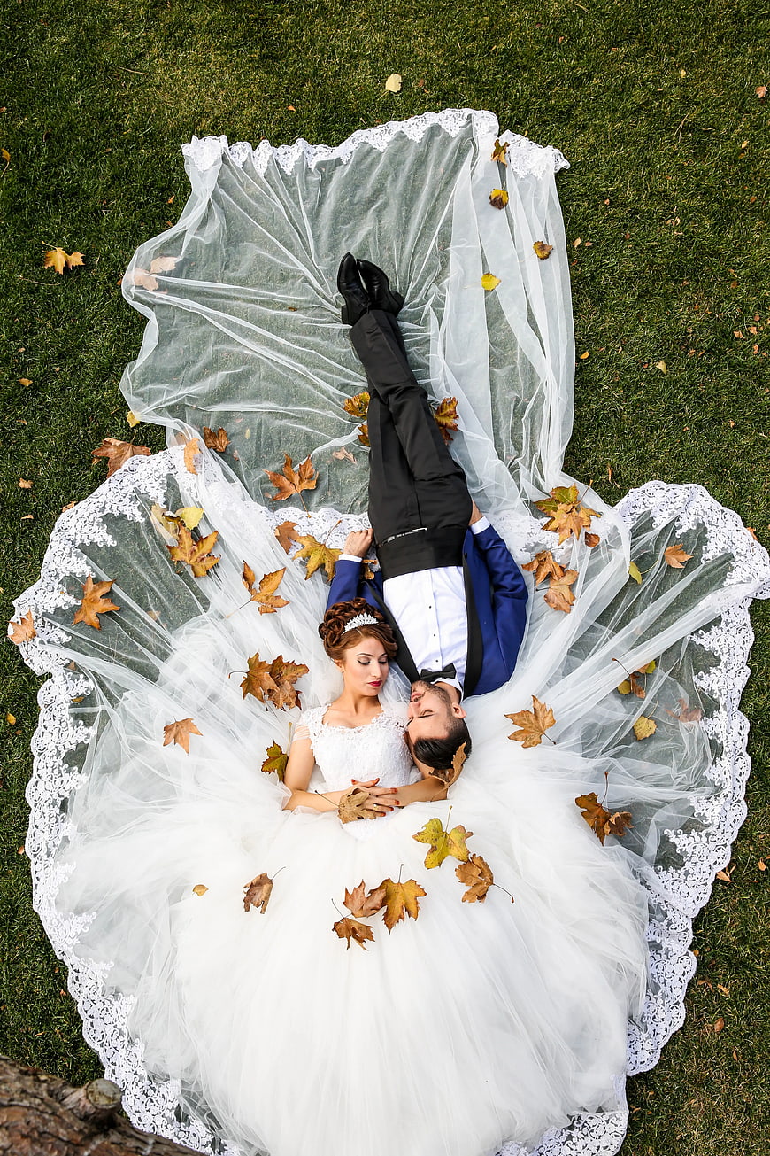 Aerial View of Bride and Groom Lying on Grass with Autumn Leaves
