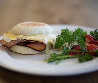 Breakfast sandwich with egg, ham, and cheese on a white plate
