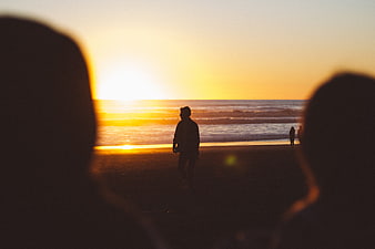 Silhouetted Figures Watching Golden Sunset on Beach
