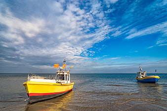 Two colorful fishing boats anchored on a sandy beach under a dramatic blue sky