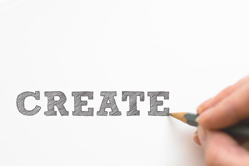 Hand writing CREATE with pencil on white paper