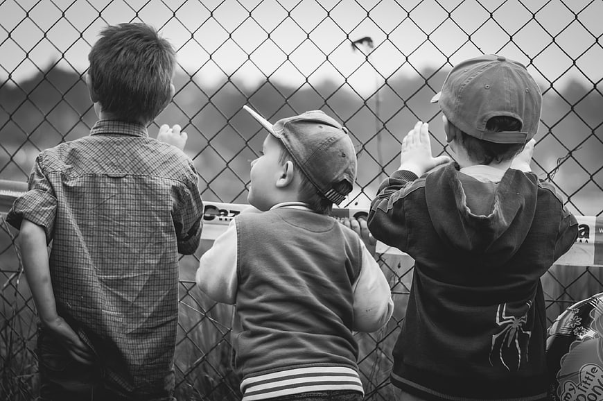 Three Young Boys Looking Through Chain Link Fence