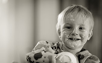 Happy toddler boy with messy face eating yogurt