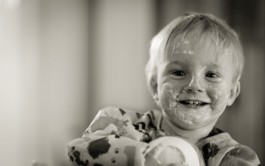 Happy toddler boy with messy face eating yogurt