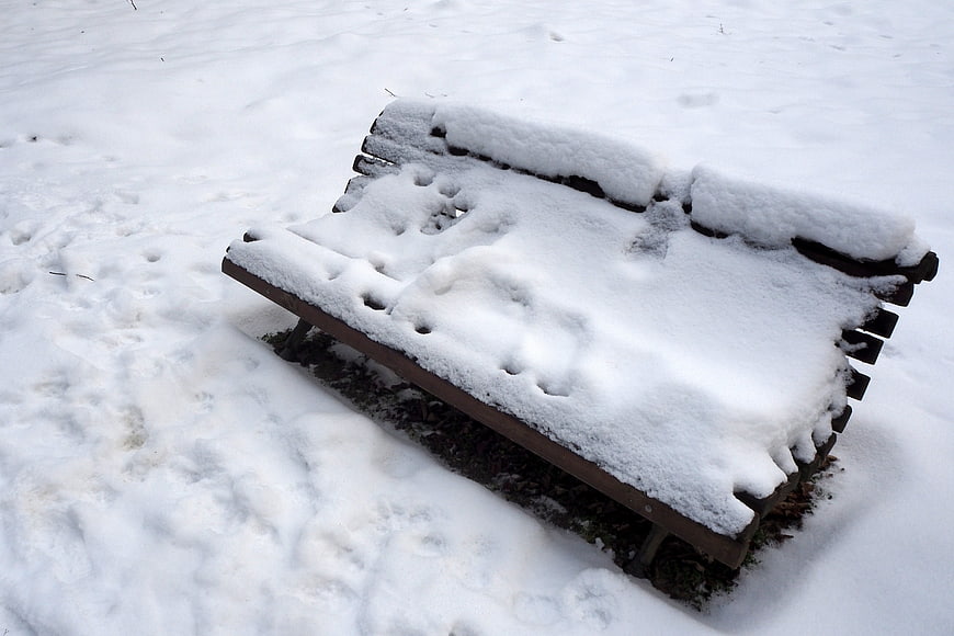 Snow-covered wooden park bench in winter landscape