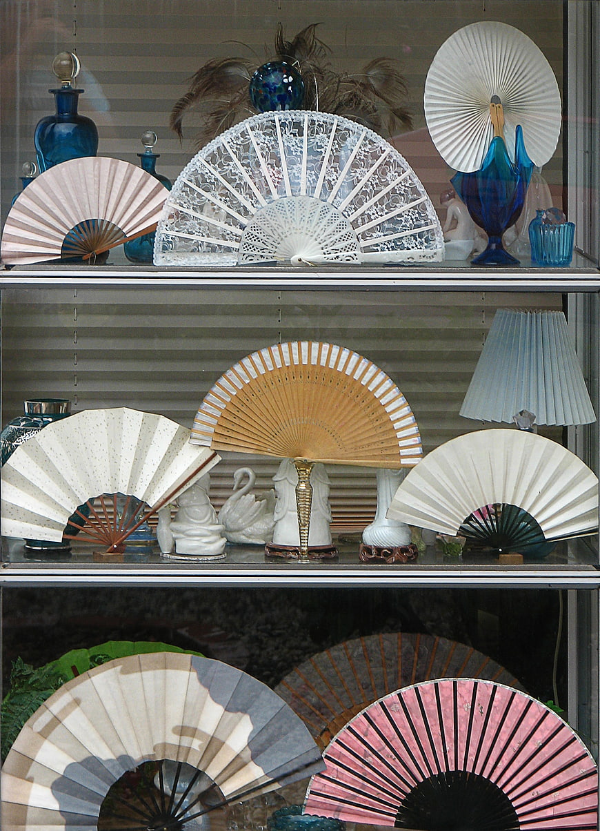 Vintage hand fans displayed on glass shelves in a shop window