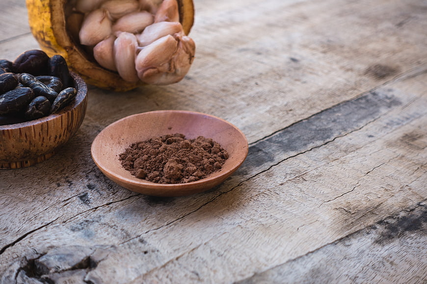 Cocoa powder, cacao beans, and fresh pods on rustic wood