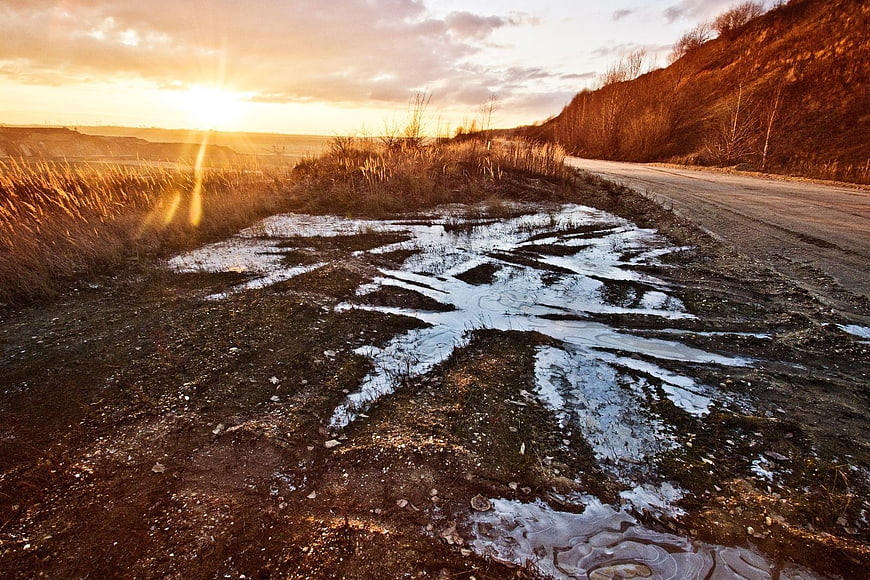 Golden Sunset Over Rural Road with Puddles and Hills