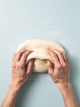 Hands kneading fresh dough on a light blue background