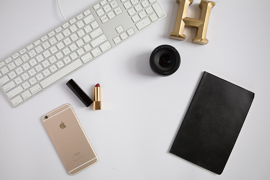 Flat lay workspace with gold iPhone, lipstick, and camera lens