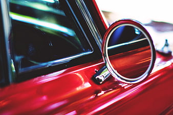 Close-up of a red car's chrome wing mirror and window