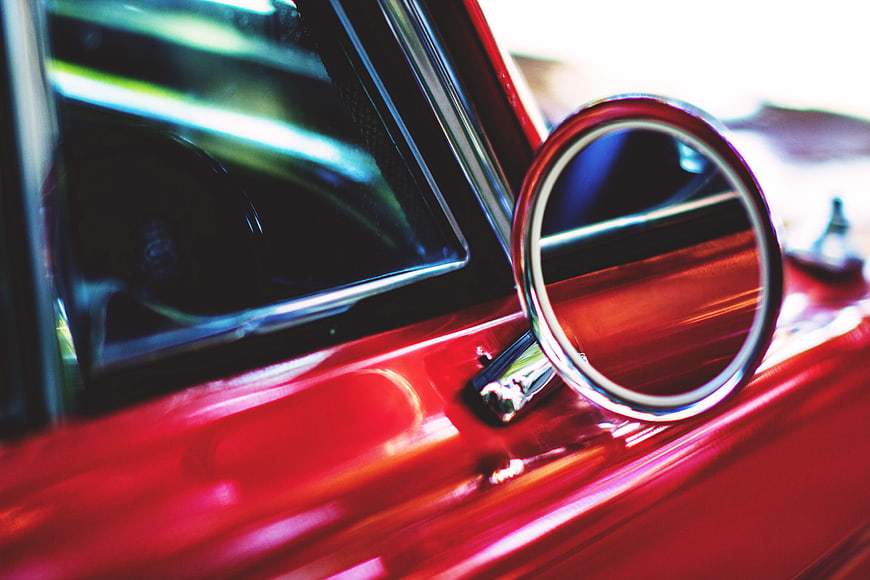 Close-up of a red car's chrome wing mirror and window