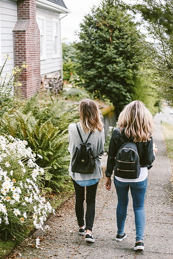 Two women walking away with backpacks on a garden path