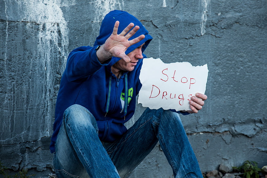 Man in Hoodie Holding Stop Drugs Sign Against Wall