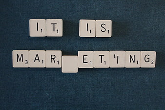 Scrabble tiles spelling IT IS MARKETING on blue background