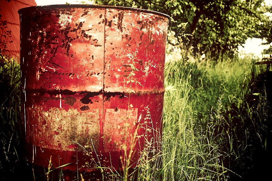 Rusty red metal barrel in overgrown grass field
