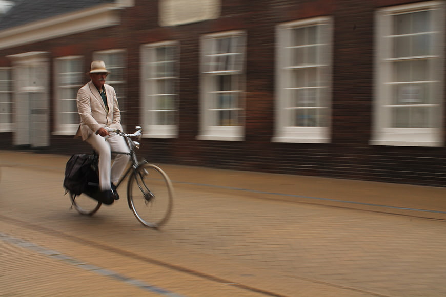 Man in beige suit riding bicycle past brick building