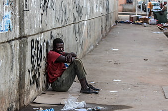 Homeless man sitting on cardboard against graffiti wall in Luanda