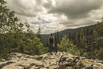 Hiker standing on rocky cliff overlooking forest mountains