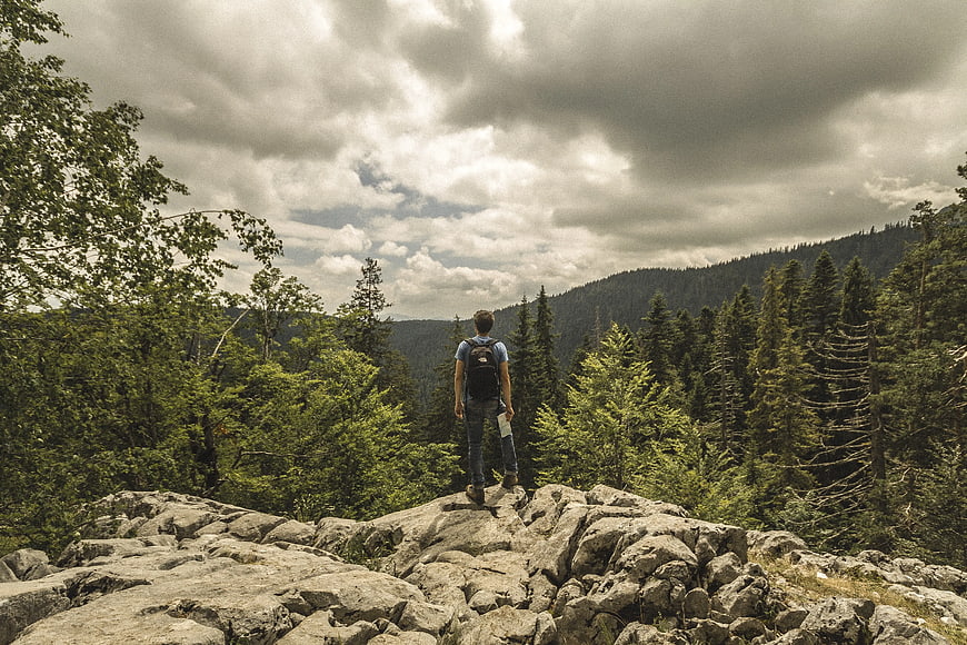 Hiker standing on rocky cliff overlooking forest mountains