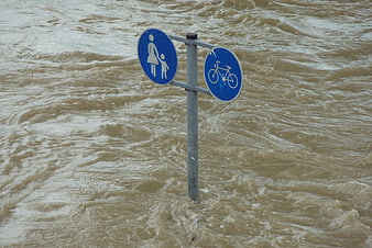 Flooded pedestrian and bicycle path sign in rushing water
