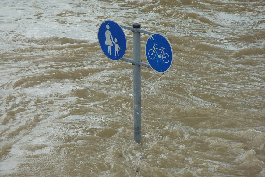 Flooded pedestrian and bicycle path sign in rushing water