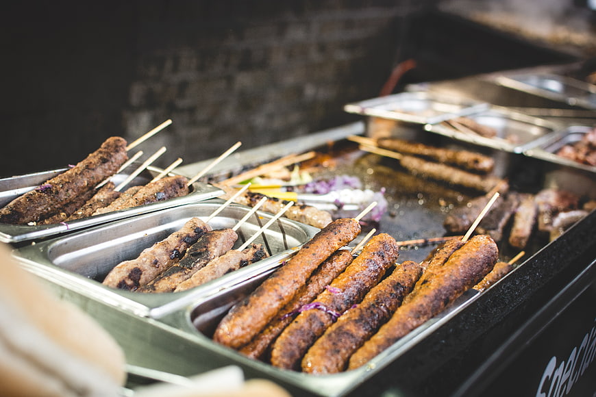 Grilled meat skewers in metal trays at street food stall