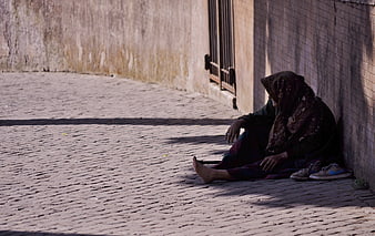 Homeless woman sitting alone on cobblestone street