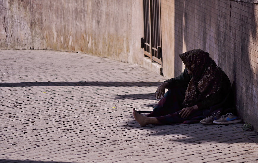 Homeless woman sitting alone on cobblestone street