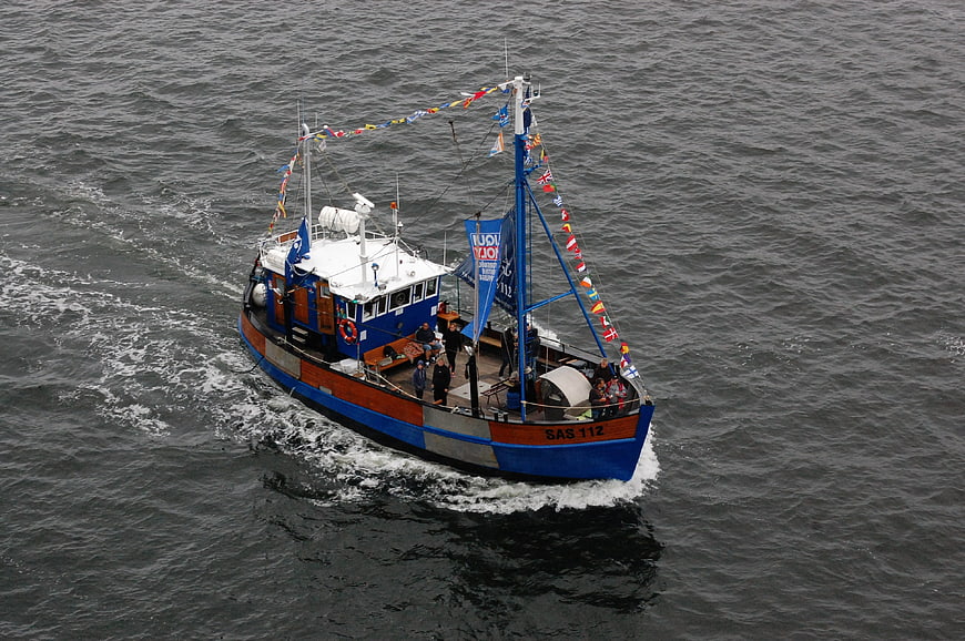 Aerial view of blue and wooden fishing boat sailing on gray sea