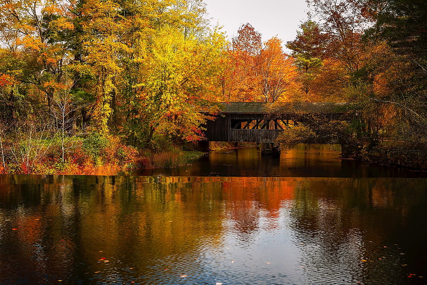 Covered Bridge in Autumn Forest with River Reflection